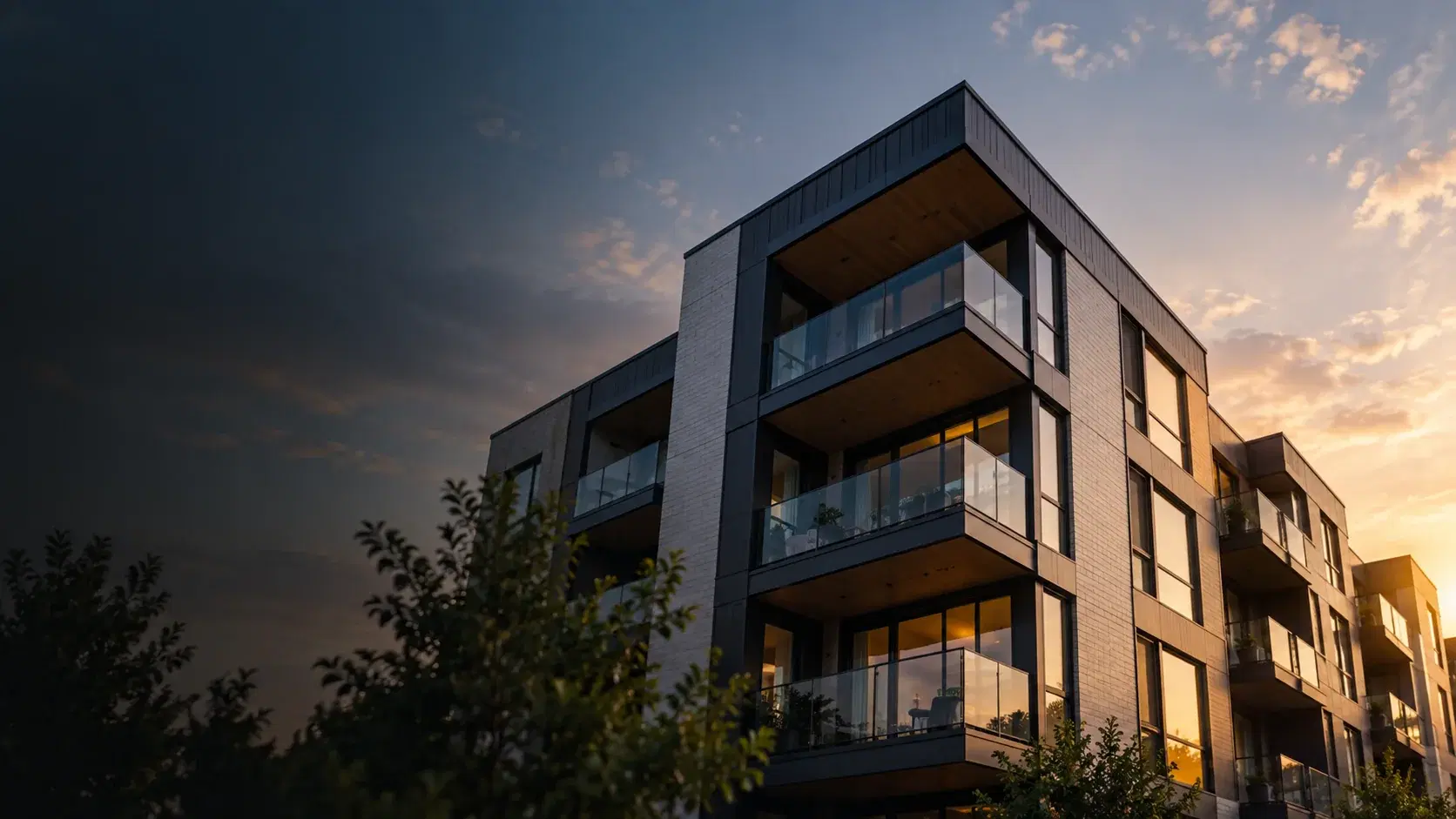 A modern low-rise apartment building at sunset, its balconies lit from within